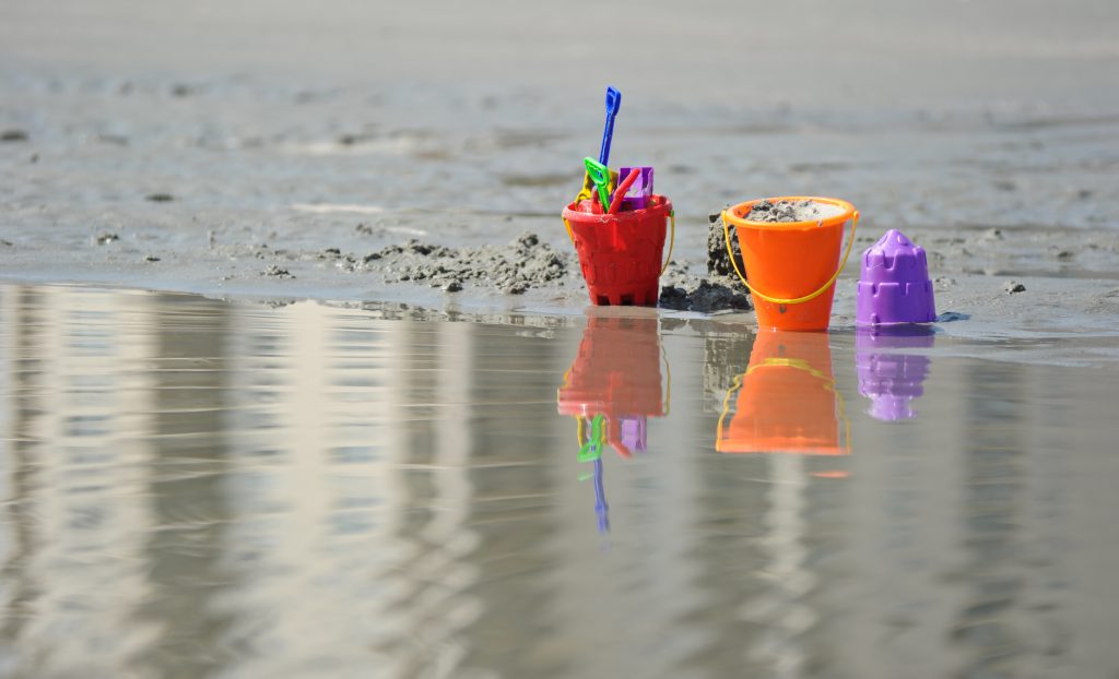 beach buckets with shovels and sand near edge of water