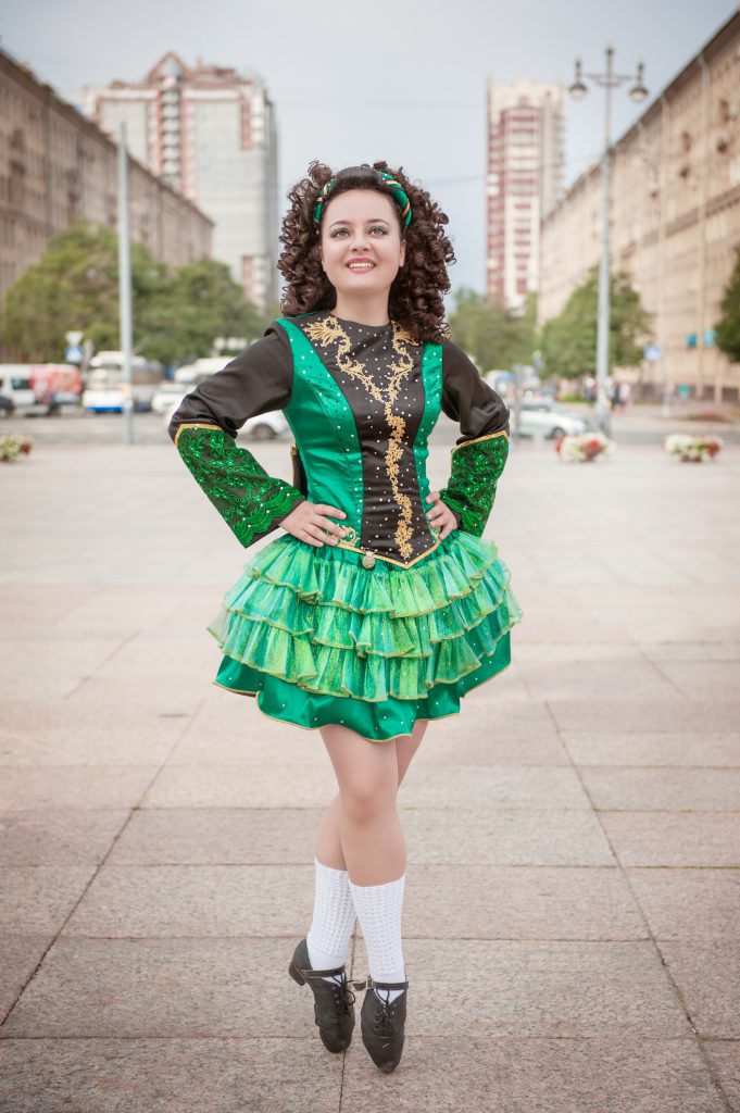 Young woman in irish dance dress and wig posing outdoor, irish clogs, white socks, buildings in the background