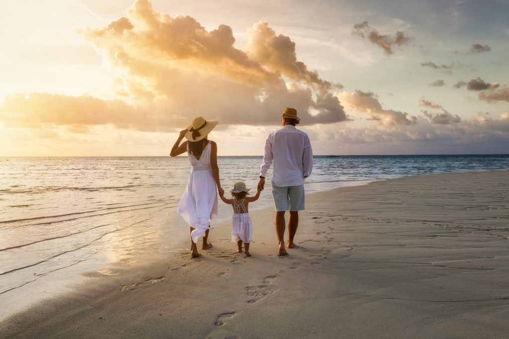 A elegant family in white summer clothing walks hand in hand down a beach during sunset tme and enjoys their vacation time