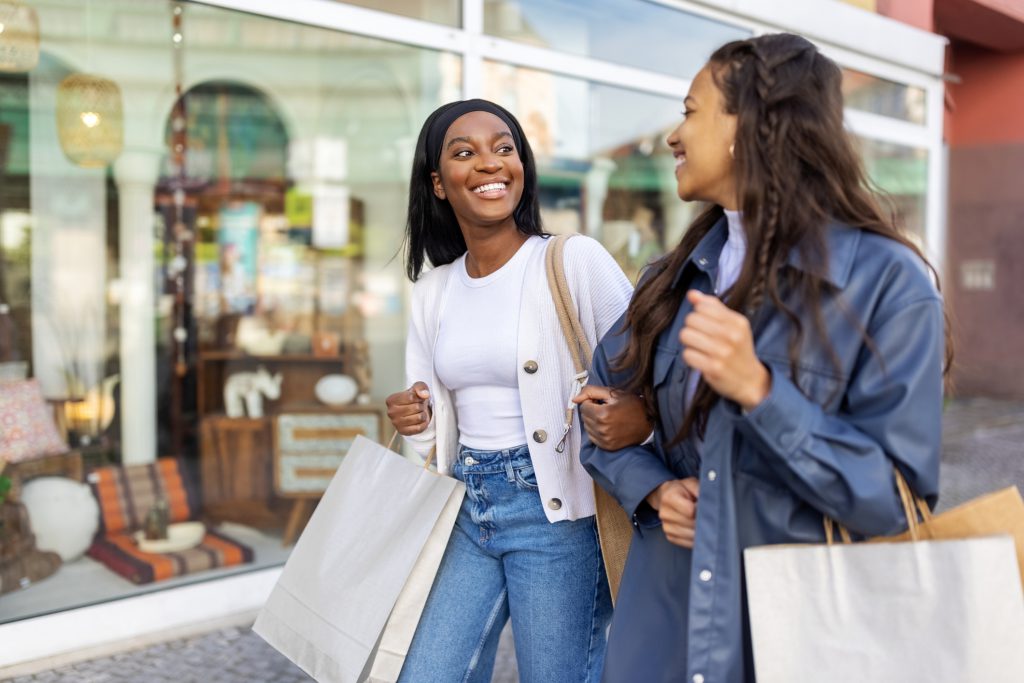 Two women friends walking and holding shopping bags. Happy young women walking in the city and talking to each other.