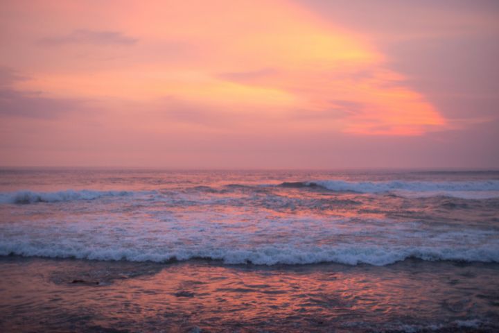 a sunset on the beach with peach and yellow skies with a few cloud coverage and the waves of the ocean gently breaking