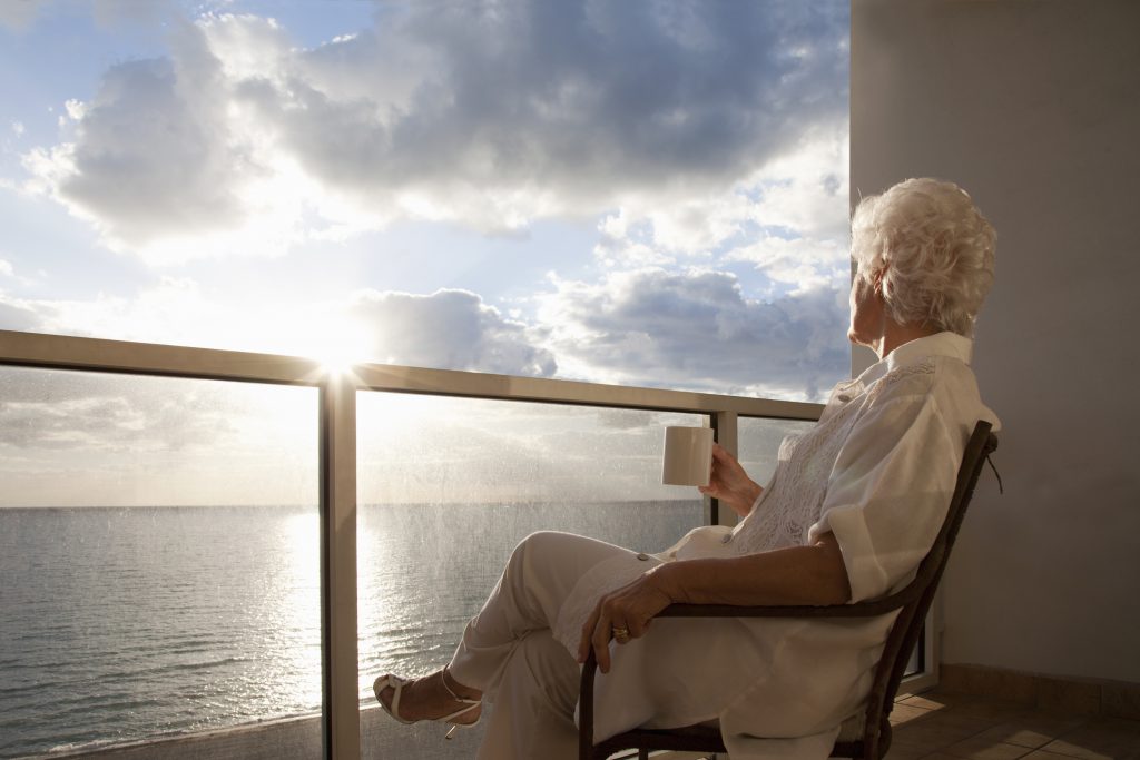 senior woman sitting on a balcony with morning coffee enjoying the sunrise over the ocean